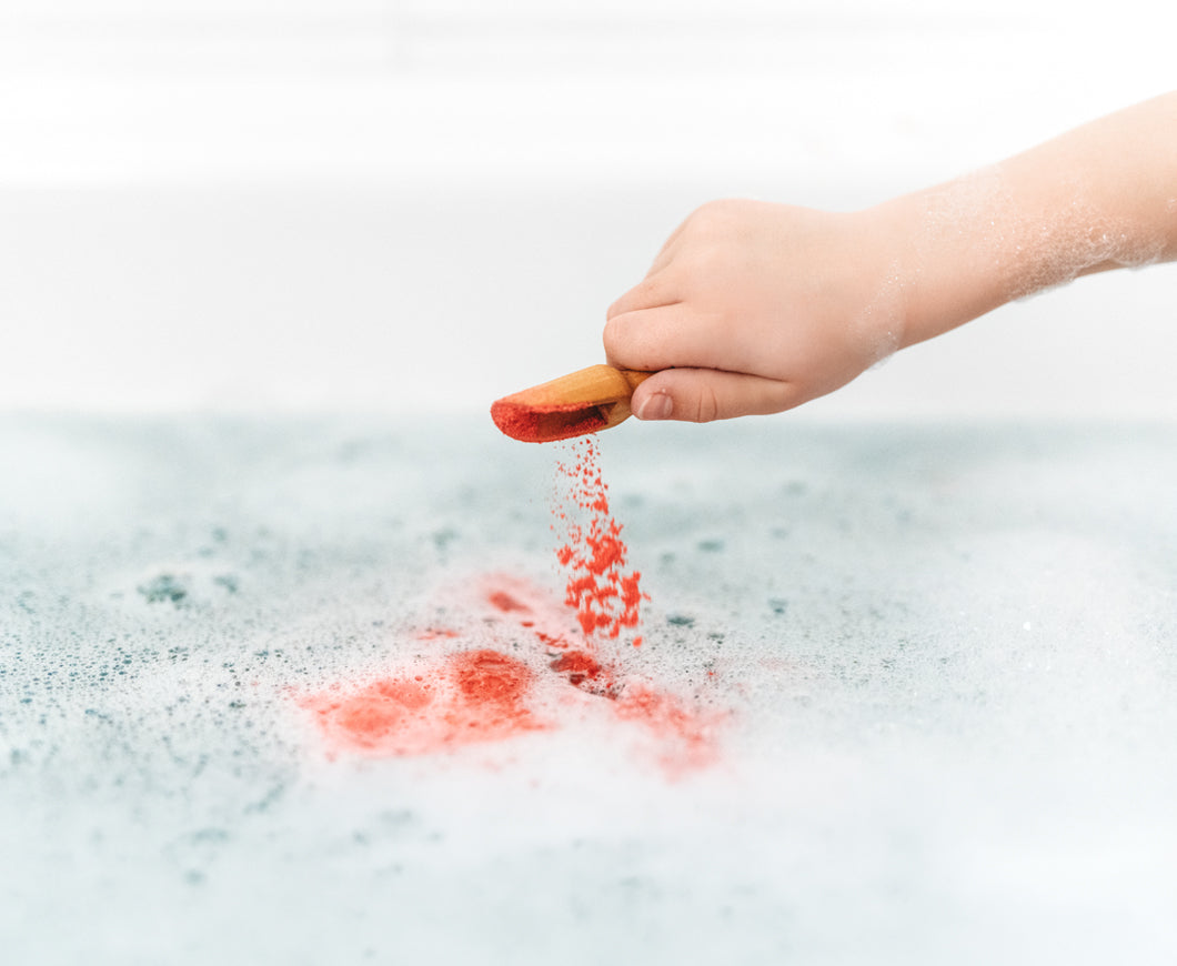 Child's hand sprinkling red dust into a bath with bubbles