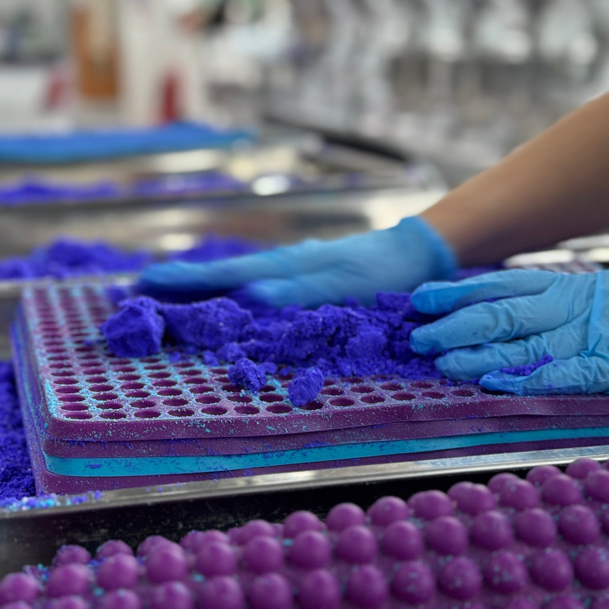 Person wearing blue gloves pressing bath bomb mix into rubber mat to make mini batg bomb pearls for potion kits