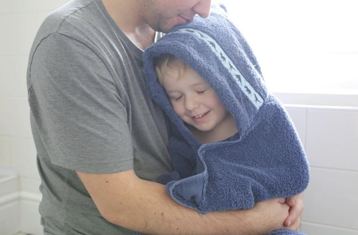 Child wearing navy blue hooded towel with Dinosaurs hooded towel enjoying a cuddle with his dad 