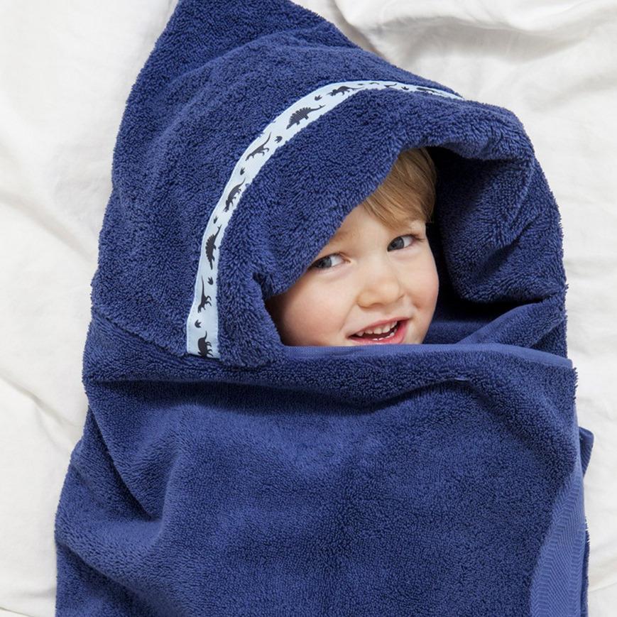 Child laying on bed with navy blue hooded towel with Dinosaurs trim