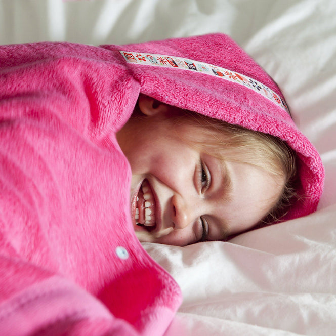 Girl laying on bed smiling snuggled in a pink hooded towel with owl trim