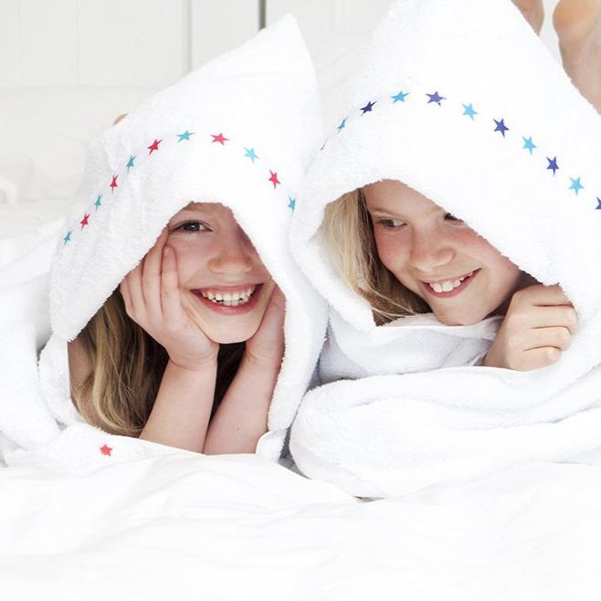 Two sisters laying next to each other wearing matching white hooded towels with a star trim