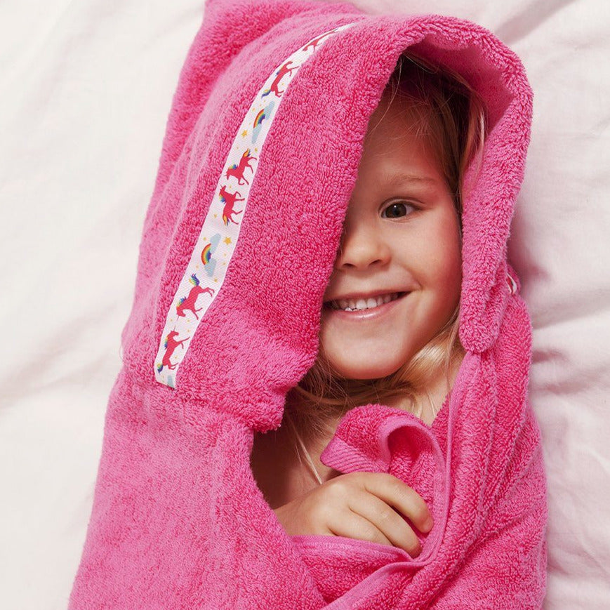 Child snuggled in pink hooded towel with unicorn trim 